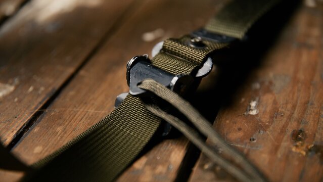 A close view of an olive drab tactical sling adjustment buckle featuring durable nylon webbing and a metal fastener component resting on a worn wooden table for professional gear display