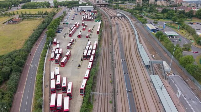 Electric buses charging at Lea Interchange depot as drone flies forward above London bus yard beside railway lines, roads, showcasing public transport infrastructure and clean energy fleet operations.