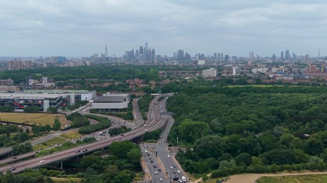 London skyline drone pullback from the City of London, revealing the Shard, the Gherkin and BT Tower under overcast skies, with green parkland and roads in the foreground.