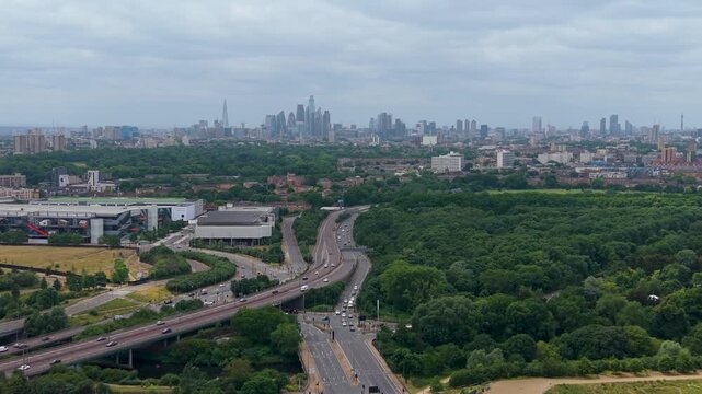 London skyline aerial tracking over the A12 toward central city, revealing the Shard, BT Tower and dense urban buildings under overcast summer skies.