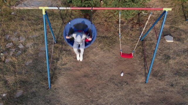 Aerial view captures a child enjoying a swing, emphasizing movement and outdoor recreation