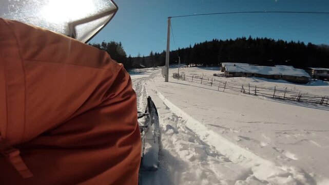 Snowmobiler rides along a powdery trail surrounded by tall, leafless winter trees