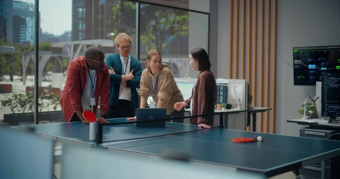 Diverse Young Software Team Meeting of Programmers and Designers Gathers Around a Laptop at a Table Tennis Setup, Collaborating on App Code, Engineering Meeting and Cybersecurity in a Modern Office.