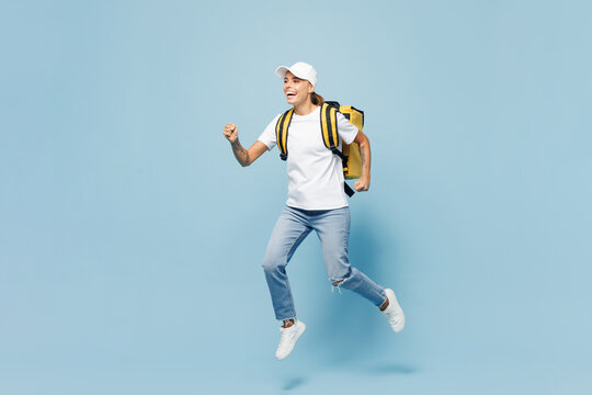 Full body delivery employee woman wear white cap T-shirt uniform yellow thermal food bag backpack workwear work as dealer courier jump isolated on plain pastel blue background studio. Service concept.