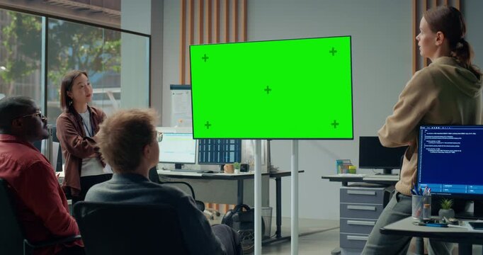 Office Meeting Presentation: Young Woman Presenter Guides Diverse App Engineers Around Large Green Screen Chroma Key Display, Reviewing Coding, Cybersecurity, AI Interface Strategy