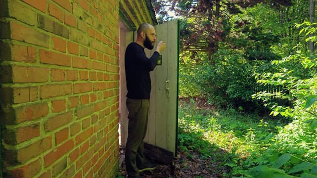 Metal mug with camping food being eaten from by a bearded man near an open brick door