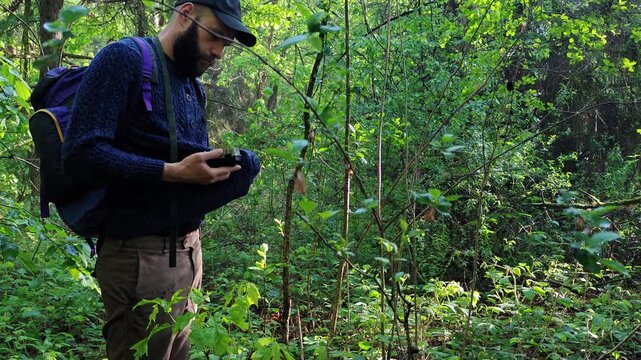 Trail camera lens being wiped with a sweater by a bearded man in the forest
