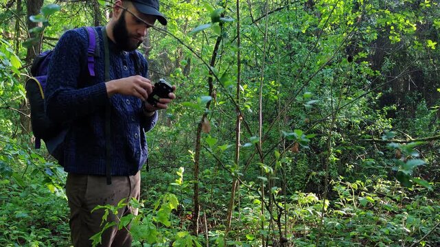 Trail camera settings being checked on a mounted tree screen by a hiker in the forest