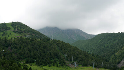 Fototapeta premium top of the mountain hidden by white rain clouds, chairlift lines on the hills, cloudy rainy weather