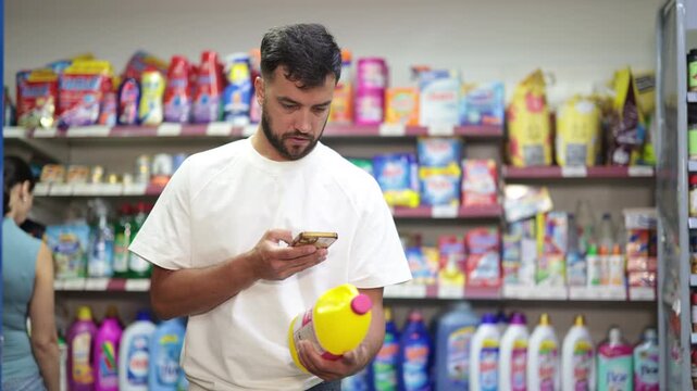Guy buyer scans qr code on liquid detergent, uses link to get additional information on Internet. Customer photographs product, searches for photo on Internet, woman shopping in background