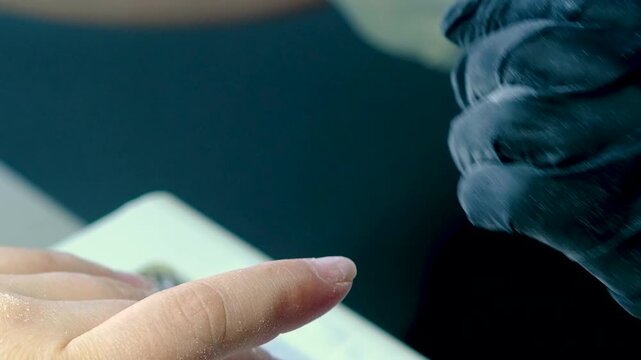Finger nail treatment, fashion, manicure making process in beauty salon Electric nail file drill in action, close up of beautician hands in black gloves working on client fingernails.