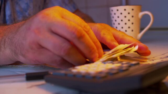 Cinematic close-up shot of writing down expense numbers from bills into a ledger book. Dark room, warm lamp light. Visualizes tax preparation, financial audit, managing personal debt and money savings