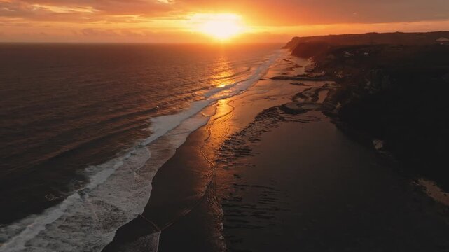 Vibrant sunset over Melasti Beach, Bali, with golden orange light reflecting across the rolling ocean waves and illuminating the rugged coastline. Travel to Indonesia. Aerial view drone flight