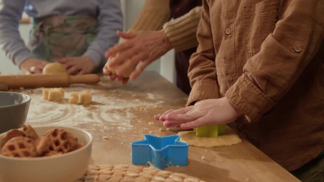 Cropped shot of child pressing cookie cutter into dough while grandparent and sibling bake in background. Perfect for family lifestyle marketing or baking product promotions