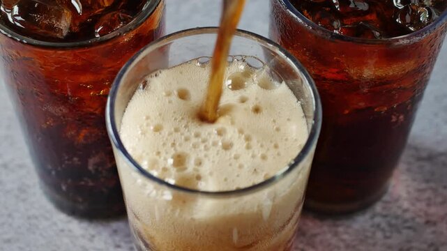 A close-up video shows dark brown cola being poured into a glass of ice, creating fizz that spreads across the ice surface, giving a refreshing and invigorating feeling.