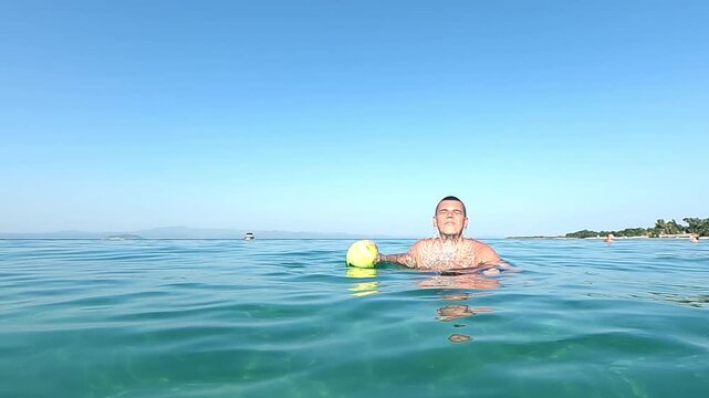 Man exit out of water and throw ball in slow motion along calm blue ocean under bright sunny sky