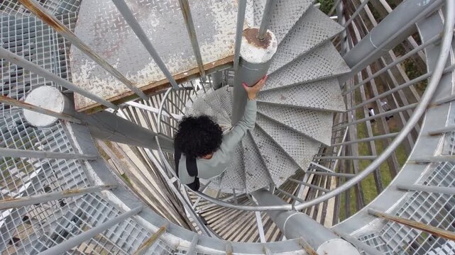 Woman descending a spiral metal staircase viewpoint platform outdoors viewed from above