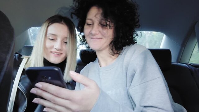 Two women sharing a moment viewing a smartphone traveling in driving car