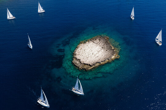High-angle aerial view of sailing yachts cruising around Taljuric rocky islet in Telascica Nature Park, Croatia