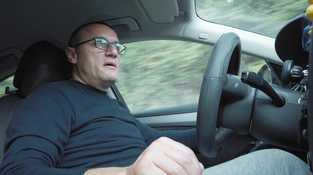 Positive singing man driving luxury car through forested area in daytime