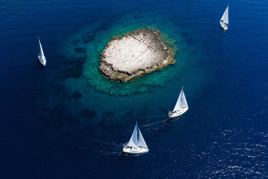 High-angle aerial view of sailing yachts cruising around Taljuric rocky islet in Telascica Nature Park, Croatia