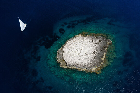 Top-down aerial view of a lonely yacht sailing by the flat rocky islet of Taljuric in Telascica Nature Park, Croatia