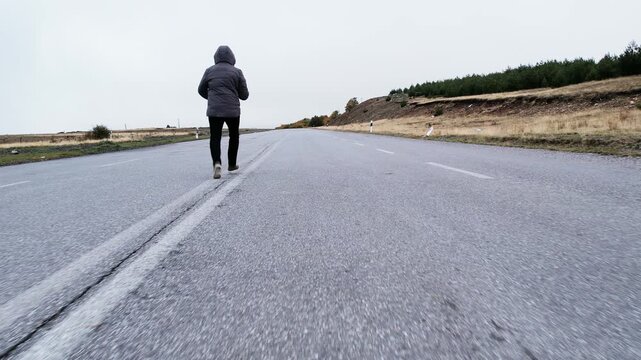 Mysterious criminal person running alone on countryside road during overcast weather