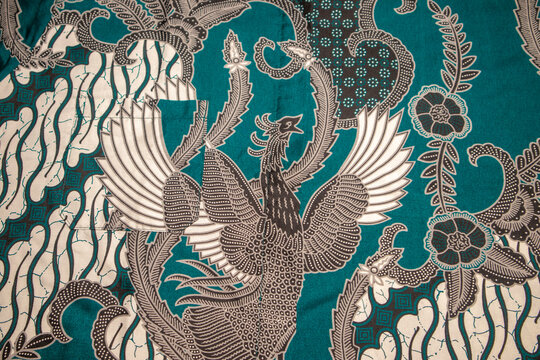 Full frame background texture of a traditional Indonesian batik fabric with turquoise green and black patterns featuring a detailed mythical phoenix bird and parang design