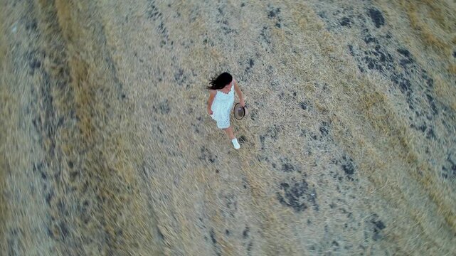 Woman in white dress walk through a dry field in summer