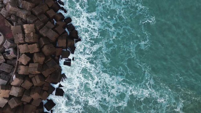 Cinematic 4K aerial drone captures waves breaking against the rocky breakwater at Miramar Beach in Ciudad Madero, Tamaulipas, with calm turquoise water stretching beyond the rocks under natural daylig