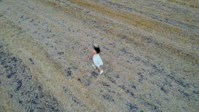 Carefree stylish woman with hat walk in harvested agriculture field in summer