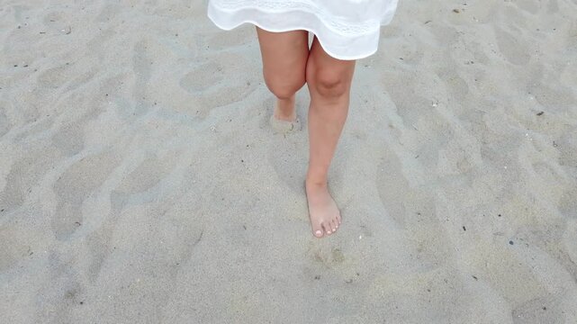 Woman walking barefoot in sand wearing a white dress on sunny day