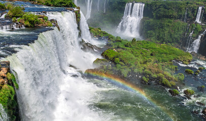 Incredible landscape of the famous Iguazu Falls with multiple cascades, water spray, and a bright rainbow bridge in the heart of the South American jungle © Yuliko