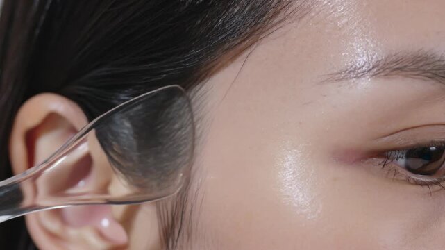 Applicator approaching temple in studio, Asian model pressing and gliding tool, showing white pad