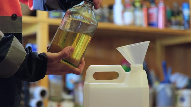 Handling oil in a workshop with a funnel and storage container in a busy environment