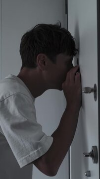Obsessive checking and OCD symptoms concept with anxious man repeatedly looking through door peephole, fear, compulsive behavior and stress, close up vertical video