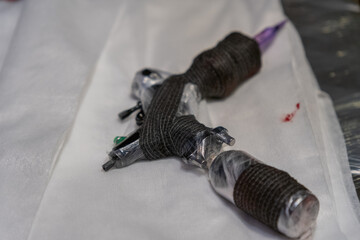 Obraz premium Tattoo machine resting on a table covered with white cloth and some splatters of ink after a tattoo session