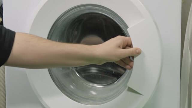 Close-up of a man's hand opening the door of a washing machine to load laundry
