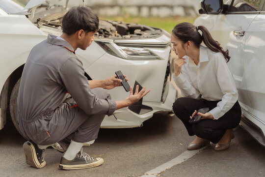 The insurance agent showed the anxious female driver at the scene of the car accident details on his smartphone, emphasizing the claims process to the Asian businesswoman after the collision.