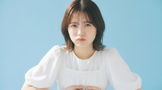 Young Japanese woman with a grumpy sulking facial expression looking at the camera on light blue background