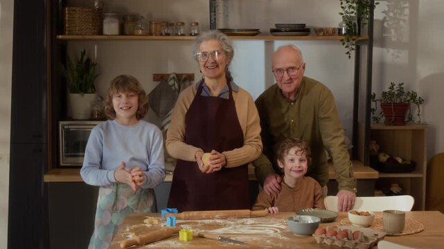 Portrait of Caucasian senior grandparents and children smiling at camera while baking in kitchen. Ideal for family lifestyle, multi-generational bonding, and home cooking advertisements