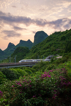 High-speed train crossing viaduct in lush karst mountains at sunset in Guangxi, China