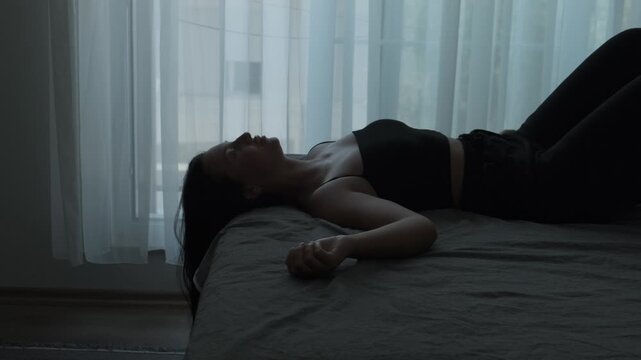 Young woman lying exhausted on bed in dimly lit bedroom