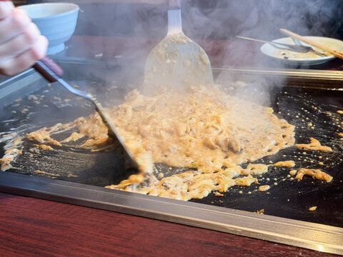 鉄板で焼いてるもんじゃ焼き。カレー味のキャベツや鶏肉をコテで混ぜている様子。