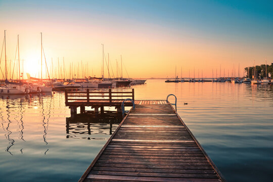 Wooden pier and sailing yachts moored in the marina on Niegocin lake during a colorful sunrise, Wilkasy, Masuria, Poland.