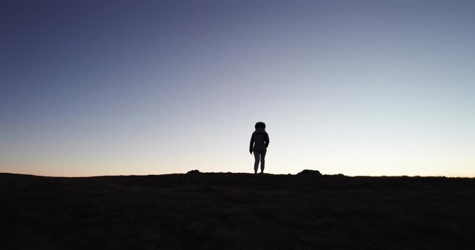 Silhouette of curly hair woman hiker hike on  mountain altitude peak with breathtaking sunset at background