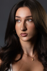 Fototapeta premium Female model posing with long dark hair, natural makeup, and a necklace in a studio