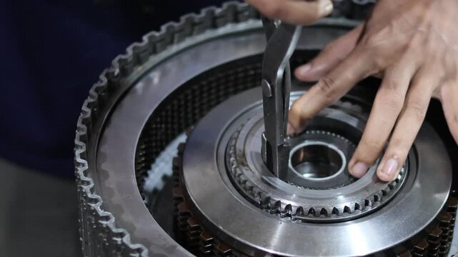A mechanic uses snap ring pliers to assemble or repair an automatic transmission gearbox component in a workshop.
