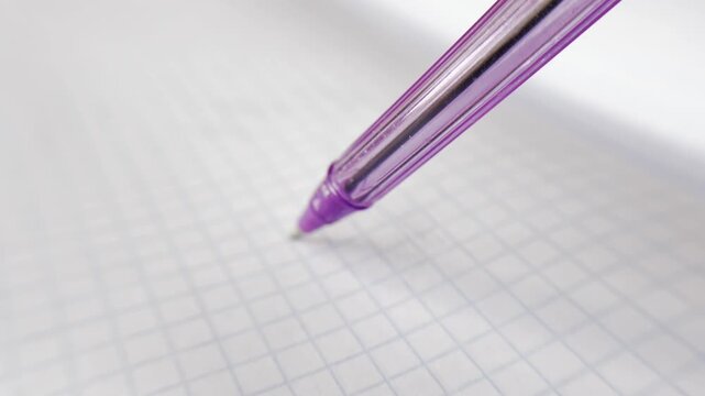 Extreme close up shot of a purple ballpoint pen lifting away from a blank sheet of gridded paper, symbolizing the end of writing, studying, or a creative process