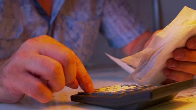 Low angle close-up of hands flipping through paper receipts under a desk lamp. Shallow DoF. Metaphor for home accounting, checking bills, tracking household expenses and family budgeting.